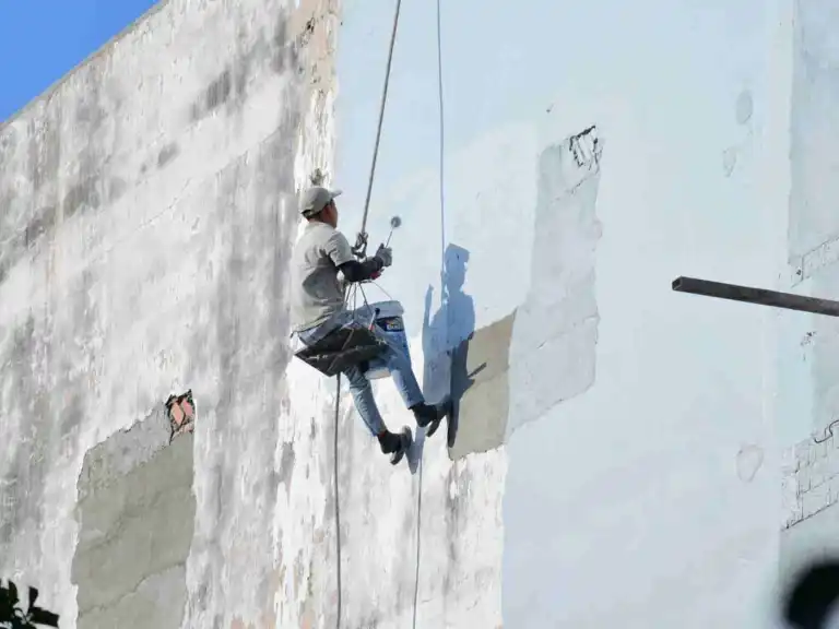 Painter suspended by ropes painting high exterior concrete building wall