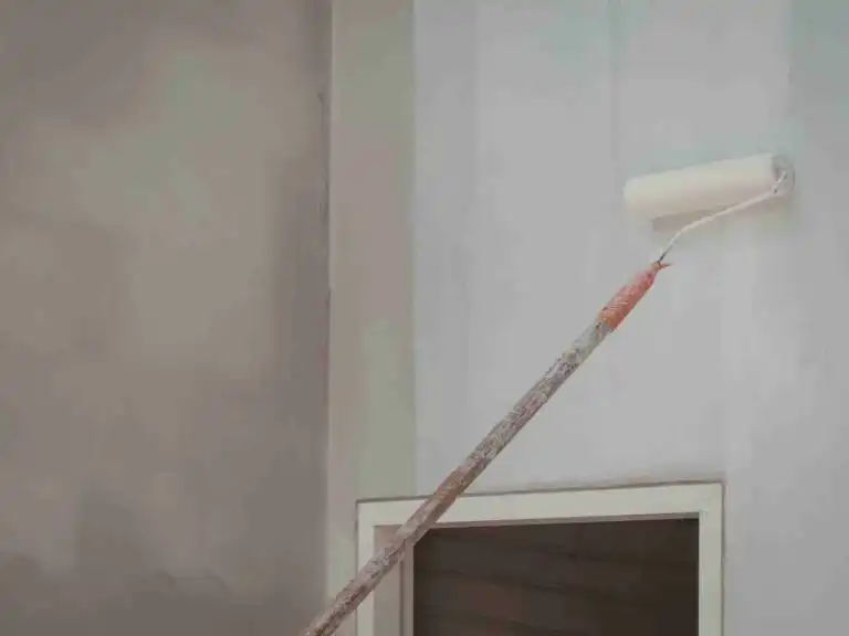 White paint roller with extension pole painting a light wall