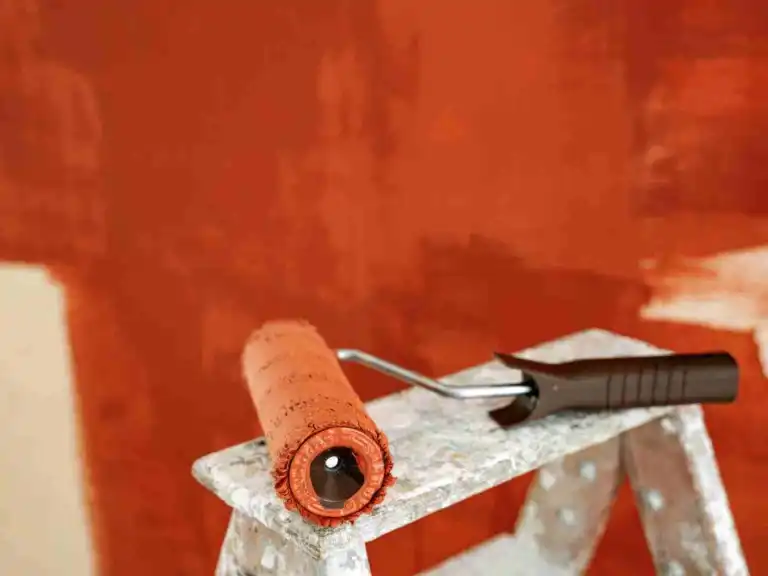 Paint roller resting on a stepladder against an orange wall