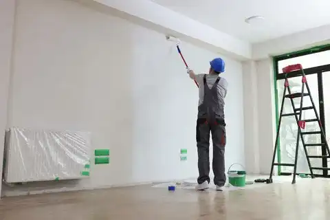 Painter in overalls and hardhat painting high wall with extension roller