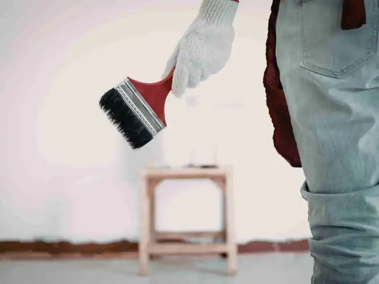 Gloved hand of a painter holding a large paintbrush in a room
