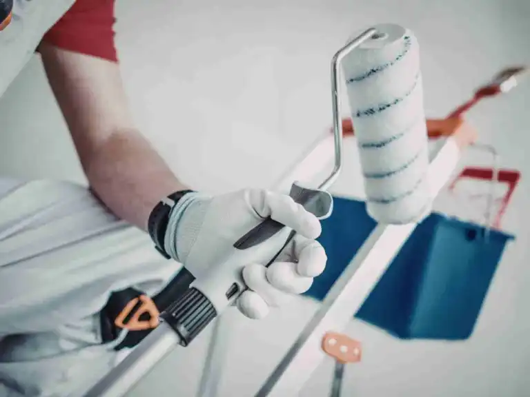 Painter holding a paint roller and tools on a ladder step