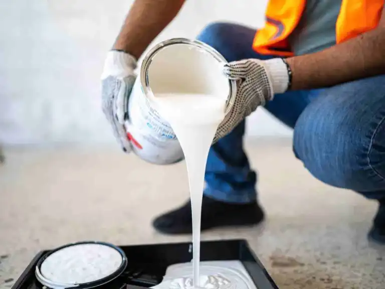 Worker in safety gear pouring white paint from a can into a paint tray