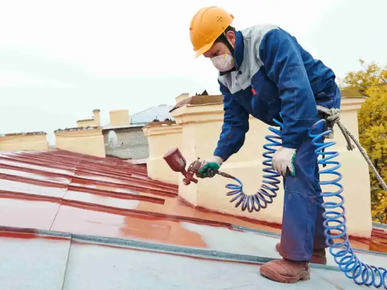 Painter using a spray gun to paint a metal roof red