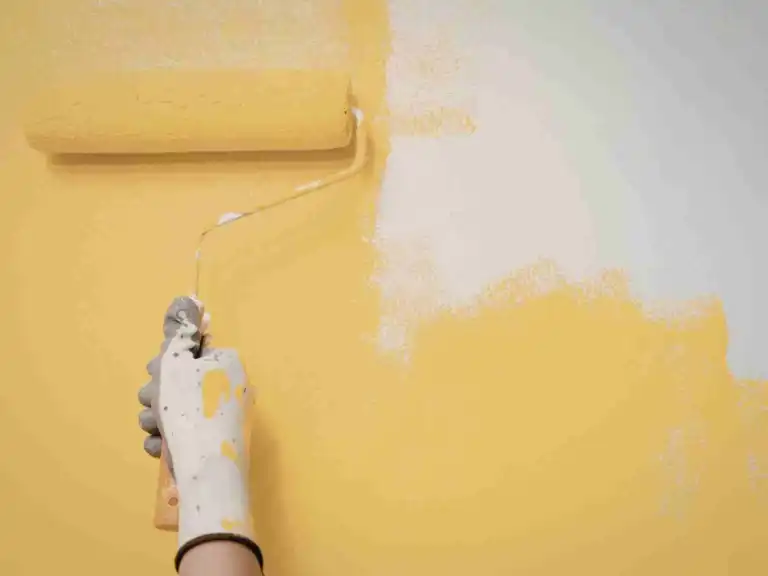 Hand with gloved hand rolling yellow paint onto a white wall surface