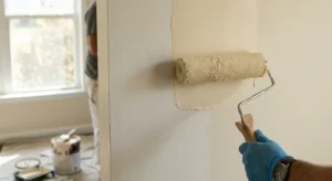 Painter applying a second coat of paint with a roller on an interior wall for even coverage, Perth painting service